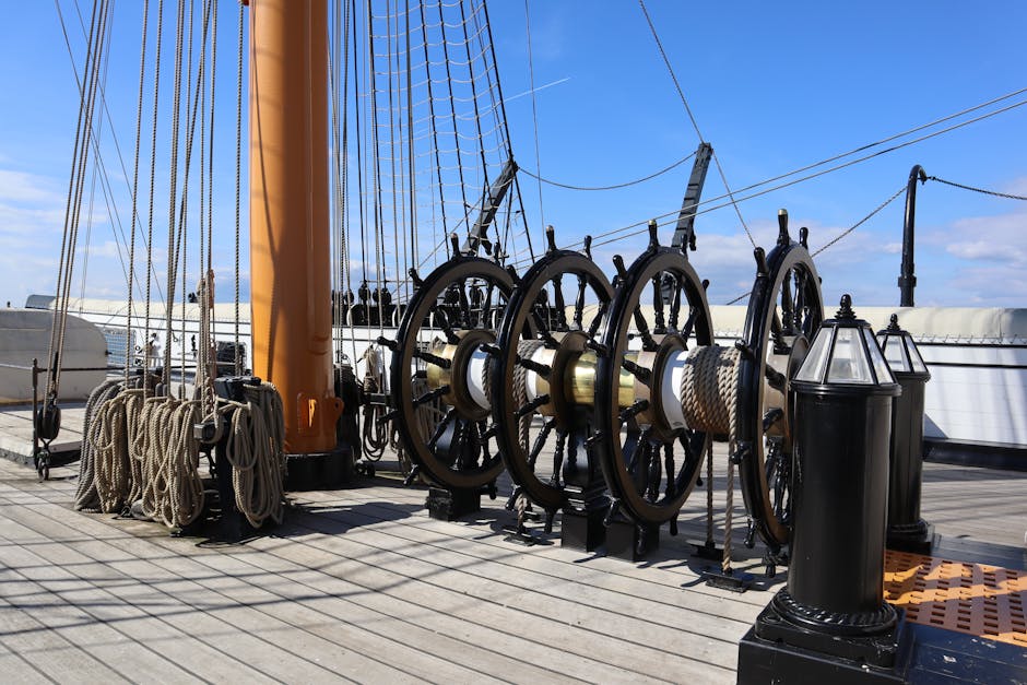 On the deck of a ship, several large black mechanical winches with white spools of rope attached are visible, with coiled ropes hanging nearby. The deck surface is made of wooden planks, illuminated b